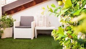 A white wicker chair with a gray cushion, a small white table with a birdcage, and green foliage in a garden setting. - Casa Erica (Bologna)