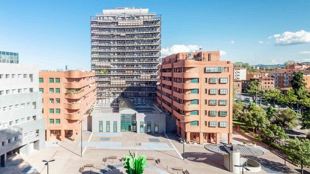 Un moderno complejo de edificios urbanos con varios pisos, un patio central y edificios residenciales circundantes.