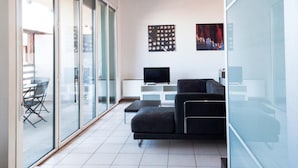 Una sala de estar moderna con un sofá, un televisor de pantalla plana y una zona de comedor con sillas y una mesa.