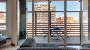 Una sala de estar moderna con un gran ventanal corredero que da a un balcón exterior con mesa y sillas.