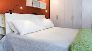 A neatly made bed with white bedding and a green throw blanket, a bedside table with a lamp, and a wardrobe with silver handles. - Bologna Centrale Flat (Bologna)