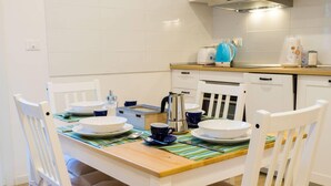 Un coin repas avec une table en bois dressée pour quatre personnes, des chaises blanches et un set de table à rayures.