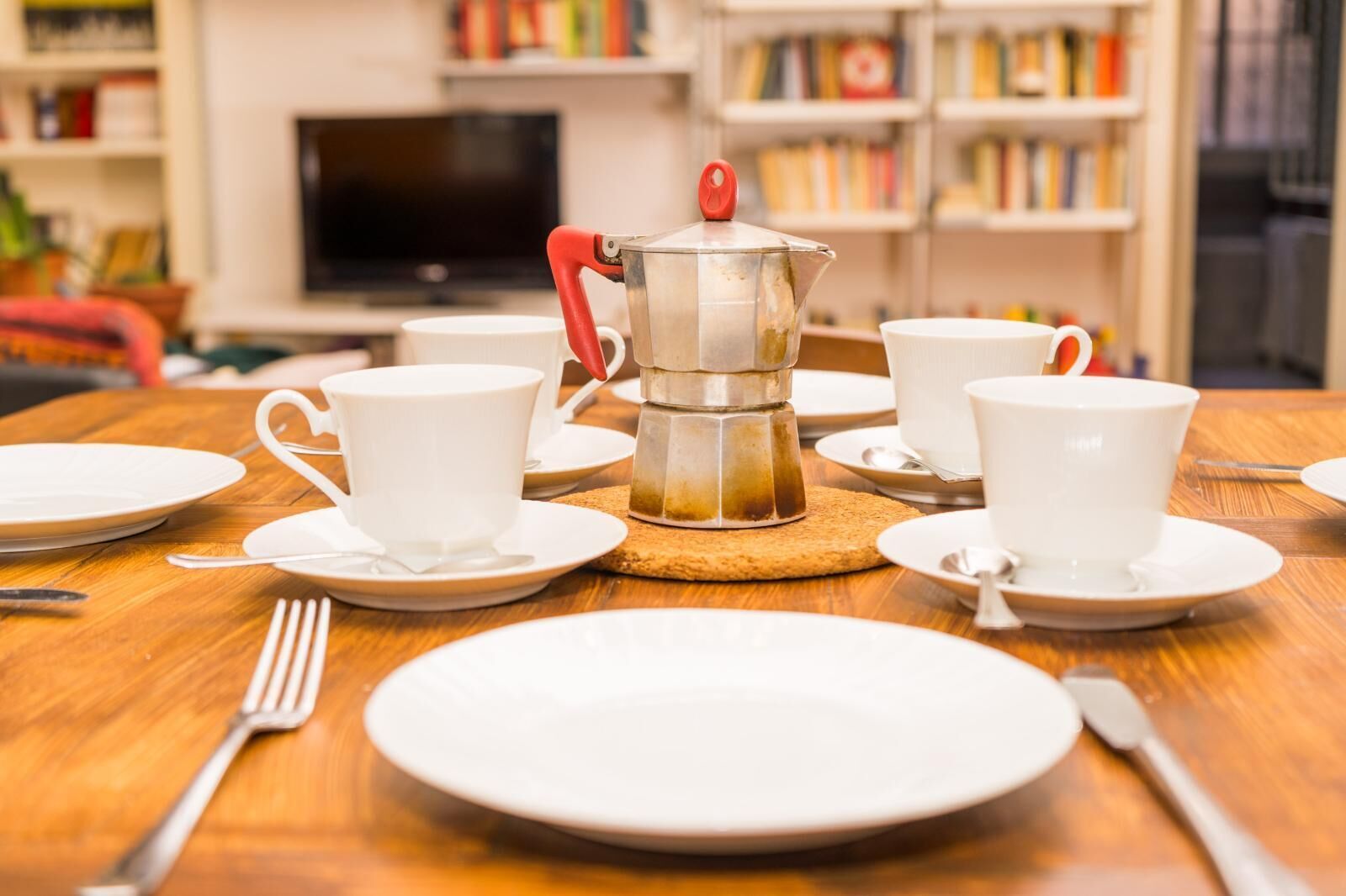Mesa de jantar posta com pratos brancos, xícaras e uma cafeteira.
