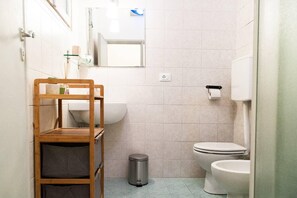 A compact bathroom with a wooden shelf, a sink, a toilet, and a trash bin. - Casa San Martino (Bologna)