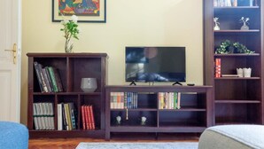 A living room with a TV on a wooden stand, surrounded by bookshelves filled with books and decorative items. - Le Mura (Bologna)