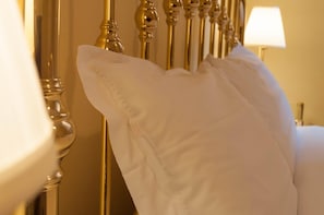 A white pillow on a bed with a gold headboard.