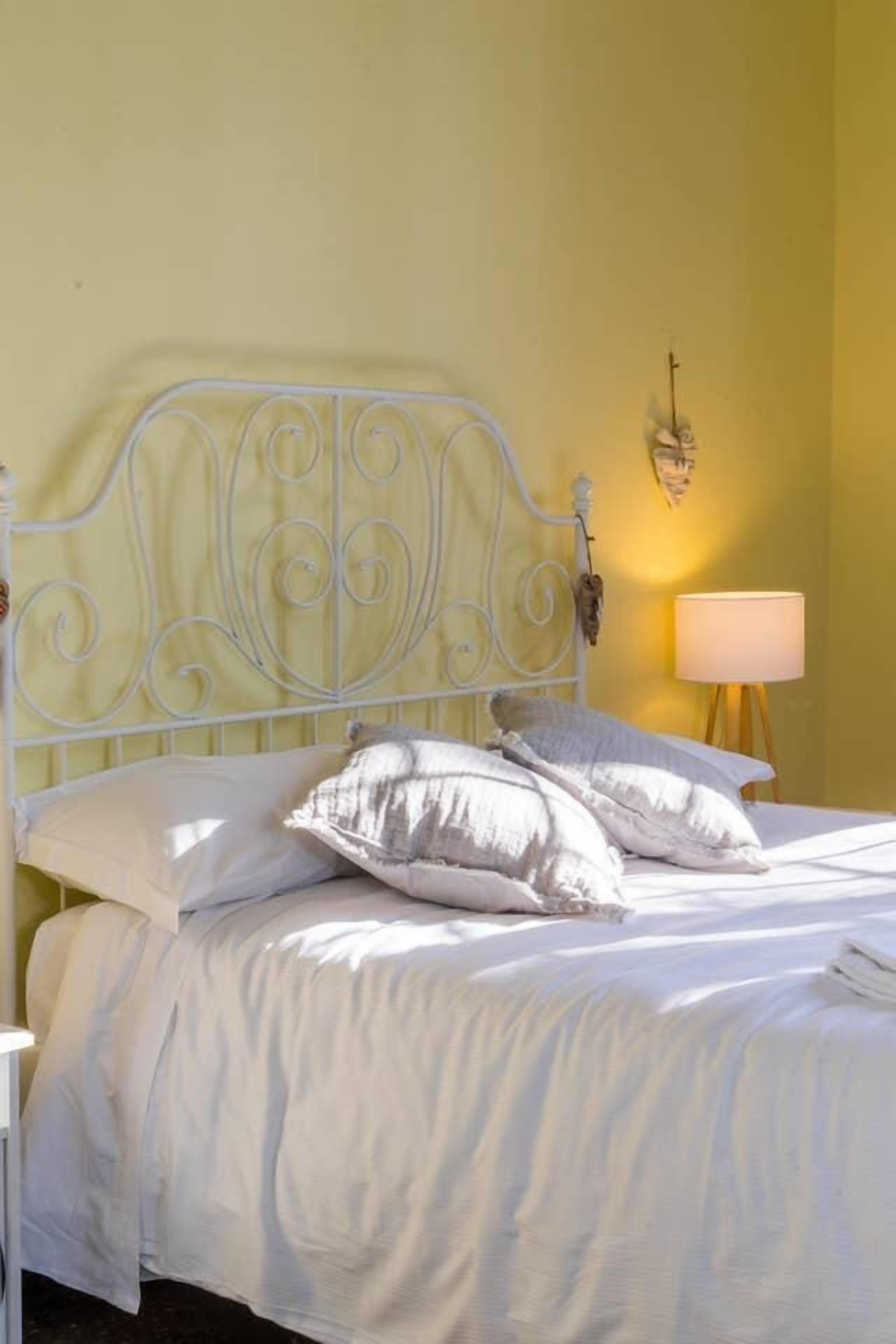 A bed with white bedding and pillows, a white metal headboard, and a bedside lamp.