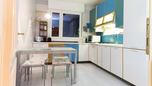 A modern kitchen with white and blue cabinets, a glass table, and a window above the sink. - Casa Luisa (San Lazzaro di Savena)