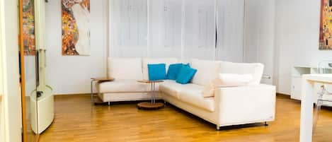 A modern living room with a white sectional sofa, two side tables, and a glass cabinet.