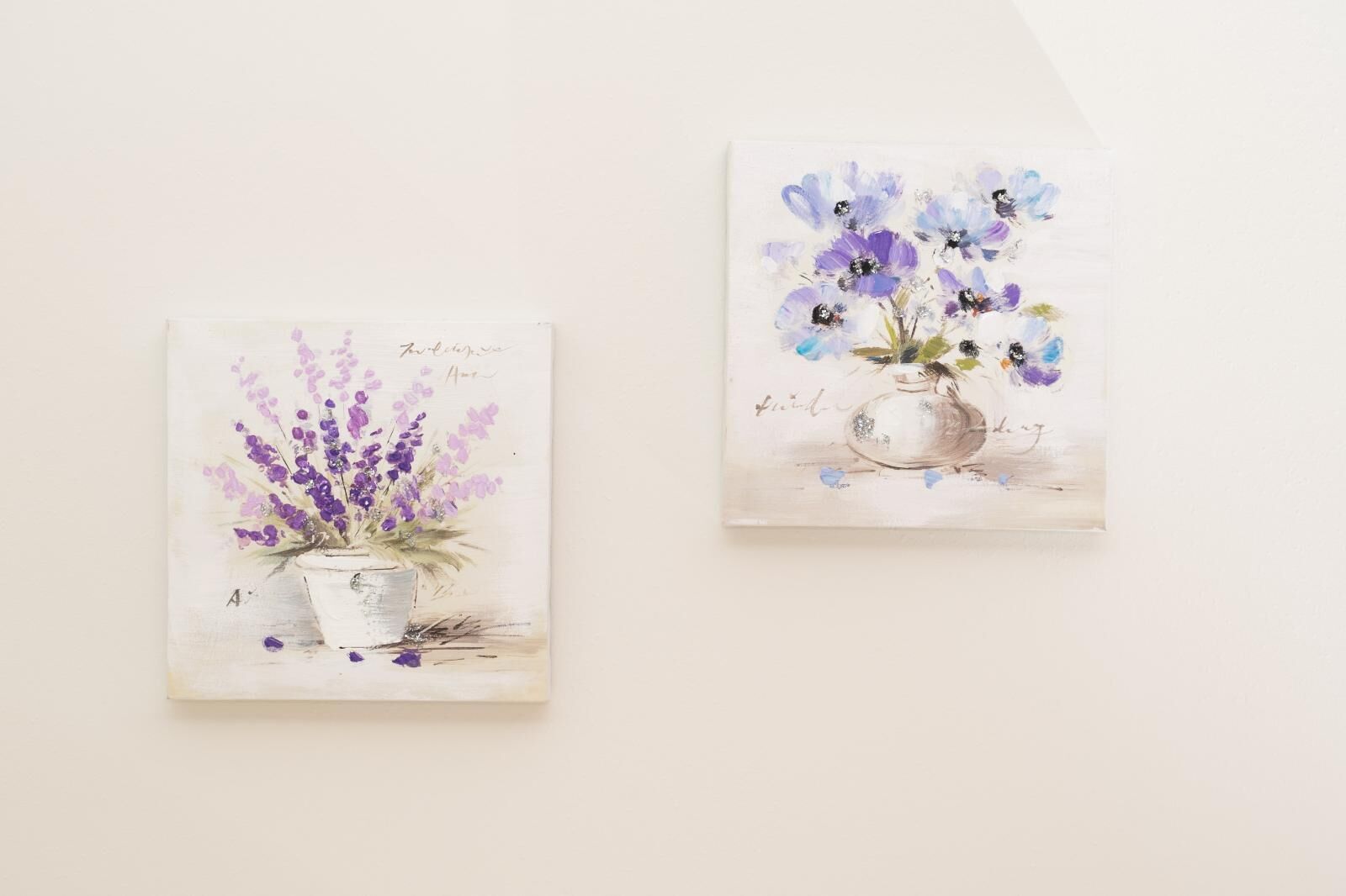 Two paintings of flowers in pots on a white wall.
