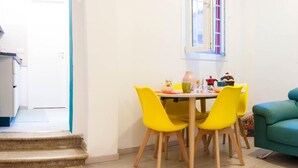 A dining area with a table and four yellow chairs, a teal sofa, and a window with curtains. - Casa Greta (Bologna)