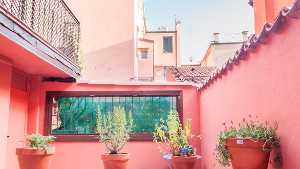 A narrow alley with terracotta pots on a ledge, a window with a green screen, and buildings with red and beige facades. - Casa Greta (Bologna)