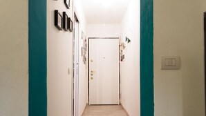 A narrow hallway with a white door at the end, teal painted walls, and a light switch on the right. - Casa Greta (Bologna)