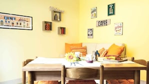A cozy dining area with a wooden table, orange cushions, and a wall decorated with vintage coffee and donut signs. - Orange Flat - Fiera District (Bologna)