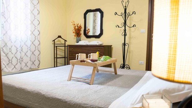 A neatly made bed with a wooden headboard, a bedside table with a candle, and a mirror on the wall. - Orange Flat - Fiera District (Bologna)