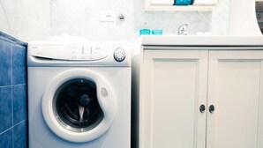 A front-loading washing machine and a white cabinet in a bathroom. - Orange Flat - Fiera District (Bologna)