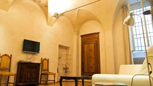 Ein Wohnzimmer mit Fernseher, Holzmöbeln, einem weißen Sofa und einem großen Fenster mit Vorhängen.