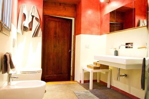 Une salle de bain avec une porte en bois, un lavabo blanc et un petit tabouret.