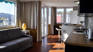 Een moderne hotelkamer met een zithoek, een eethoek, een keuken en grote ramen met uitzicht op de stad.
