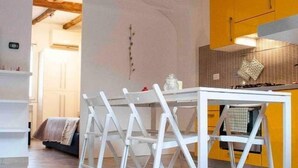 A dining area with a white table and chairs, a hanging pendant light, and a yellow kitchen in the background. - Yellow Studio (Bologna)