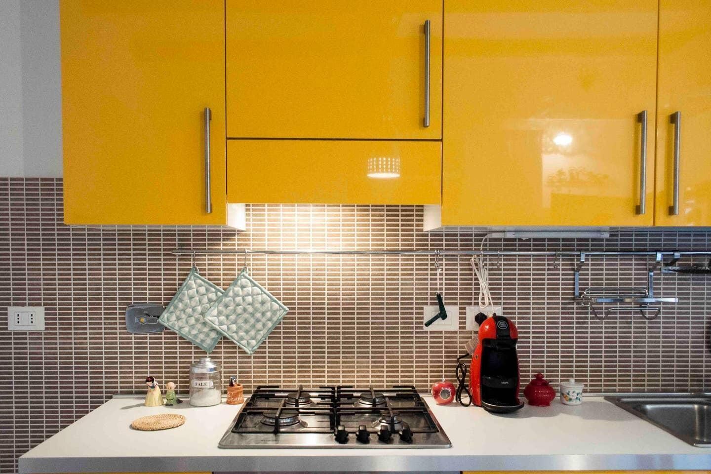 A kitchen with yellow cabinets, a gas stove, a coffee maker, and hanging kitchen utensils.