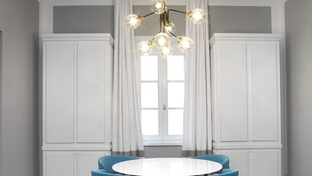 Ein Essbereich mit einem runden Tisch, vier blauen Stühlen, einer Chandelier und weiß getäfelten Wänden.