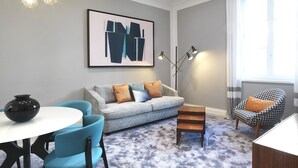 Ein modernes Wohnzimmer mit einem grauen Sofa, blauen Sesseln, einem Couchtisch und einer schwarzen Vase.