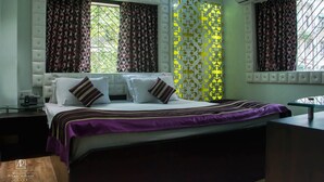 A modern bedroom with a large bed, a bedside table, and a window with patterned curtains. - Ashreen Guest House (Kolkata)