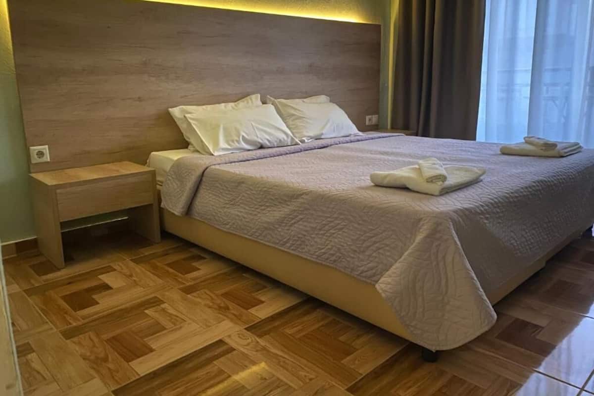 Ein ordentlich bezogenes Bett mit Kopfbrett, einem Nachttisch und einem Paar gefalteter Handtücher.