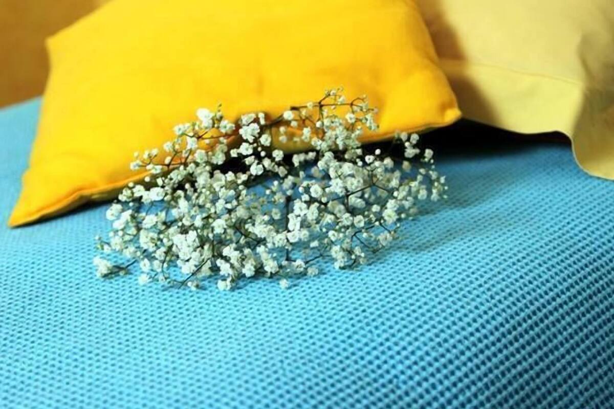 Een bed met een blauw laken en twee kussens, één geel en één beige.