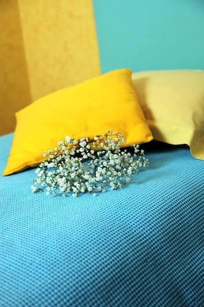 Een bed met een blauw laken en twee kussens, één geel en één beige.
