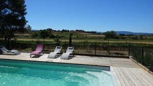 Un espace piscine avec des chaises longues et une vue sur les vignes et les collines.