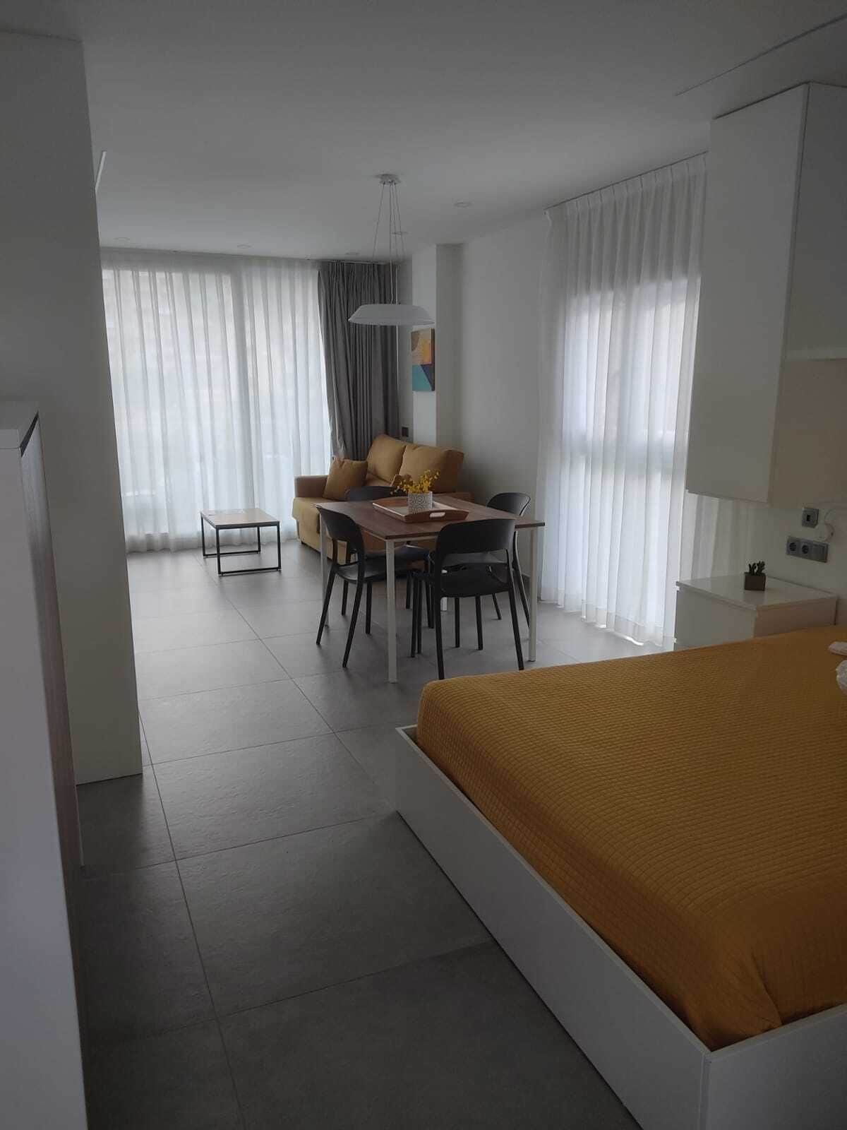 Ein modernes Hotelzimmer mit einem großen Bett, einer Essecke mit Tisch und Stühlen, einer Sitzecke mit Sofa und einem großen Fenster mit Vorhängen.