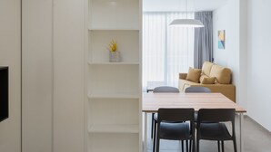 Een moderne, minimalistisch ingerichte kamer met een groot bed, een eettafel met stoelen, een bank en een inbouw kast.
