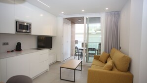 Een ruimtelijke leefruimte met een kitchenette, een bank, een eethoek en een glazen schuifdeur naar een buitenbalkon.