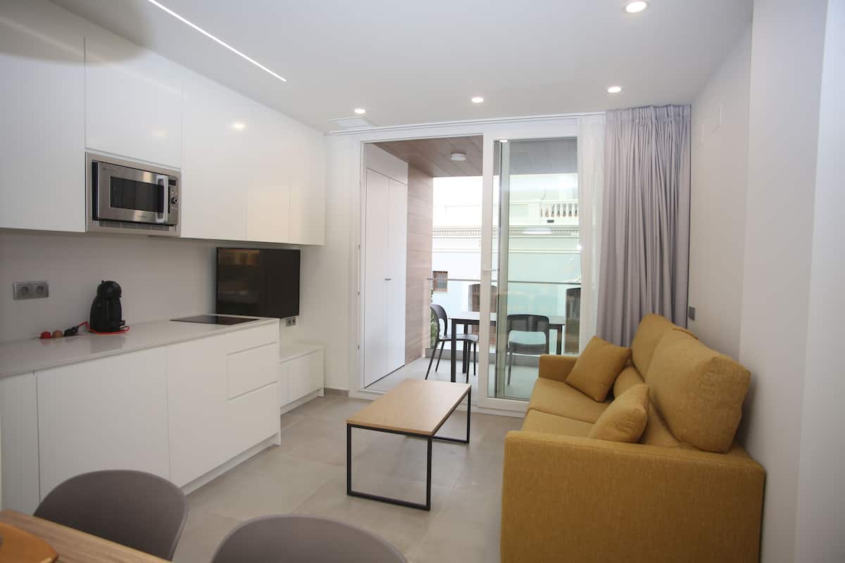 Een ruimtelijke leefruimte met een kitchenette, een bank, een eethoek en een glazen schuifdeur naar een buitenbalkon.
