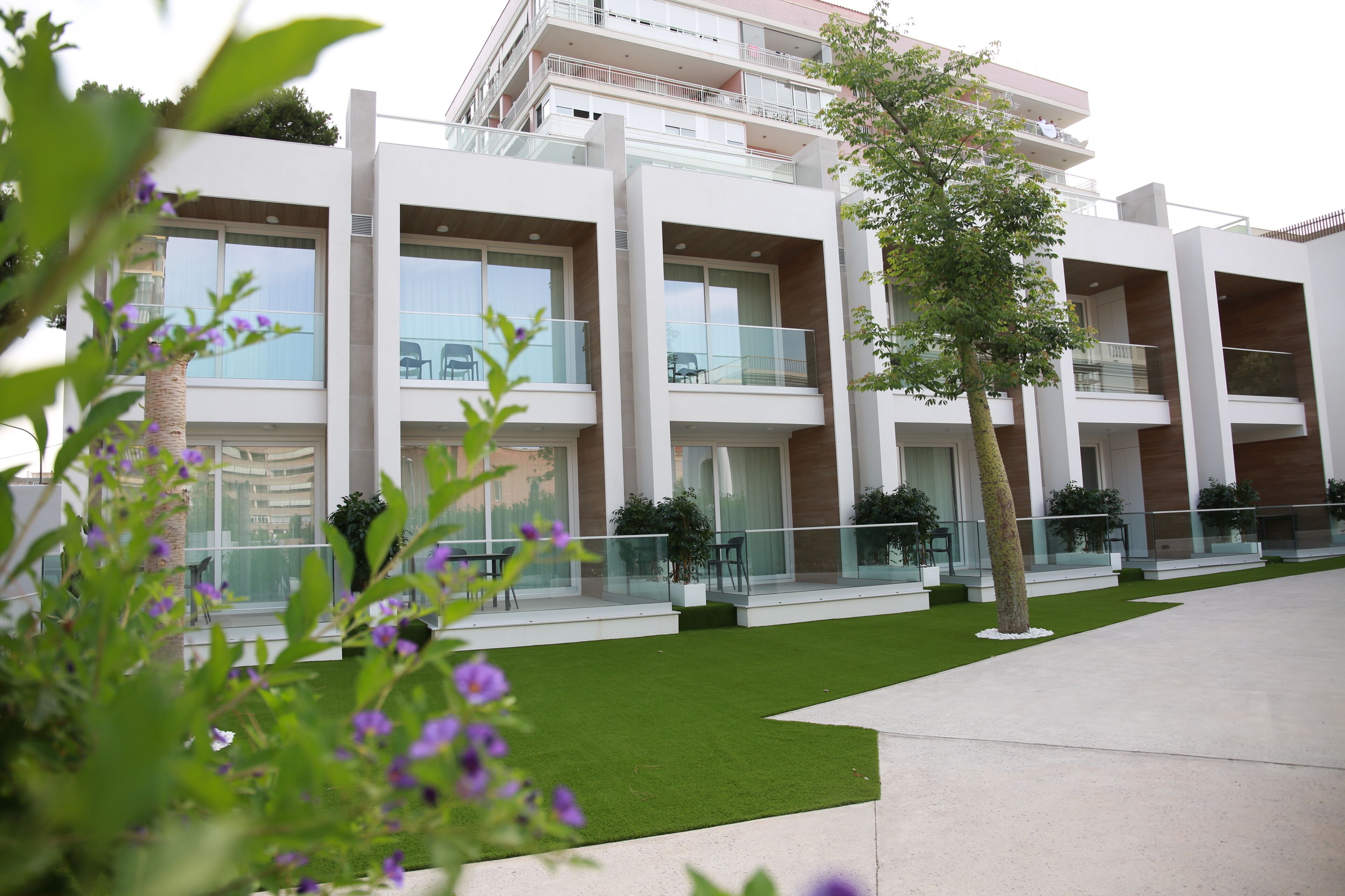 A modern multi-story hotel with balconies, a well-maintained lawn, and outdoor seating areas.