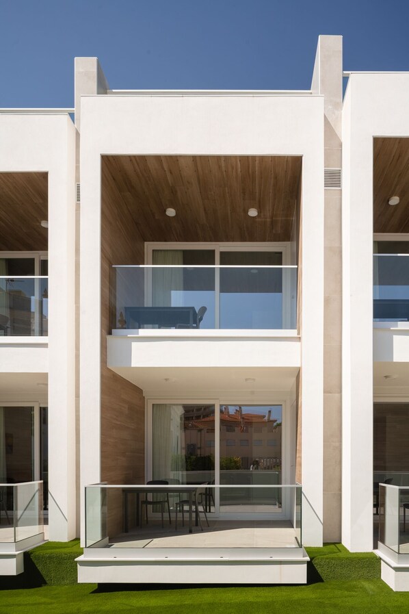 Un edificio moderno de dos pisos con un balcón en el nivel superior, ventanas amplias y techo plano.