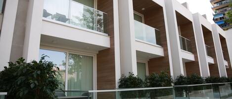 Un edificio moderno con varios balcones, barandillas de vidrio y un pequeño espacio al aire libre con una mesa y sillas.