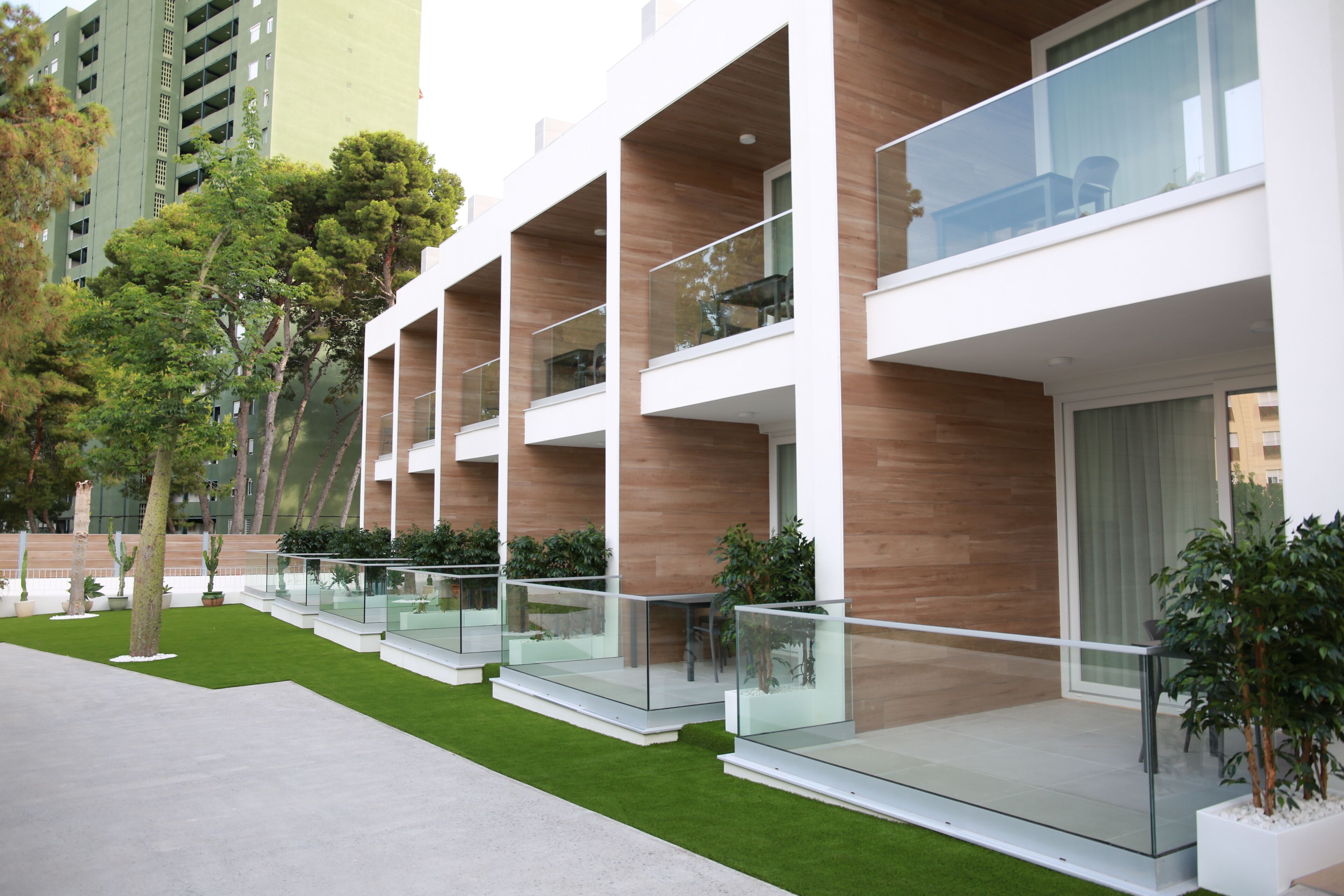 A modern building with multiple balconies, glass railings, and a well-maintained lawn.