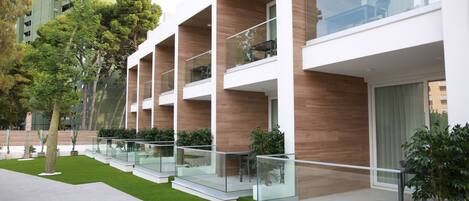 A modern building with multiple balconies, glass railings, and a well-maintained lawn.