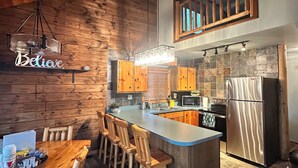 Una cucina moderna con mobili in legno, un frigorifero in acciaio inossidabile e un angolo bar con sgabelli.