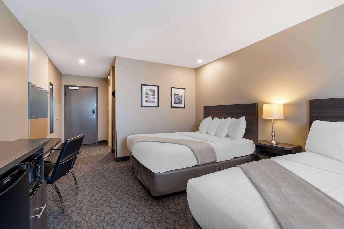 A hotel room with two beds, a desk, a chair, and a lamp.