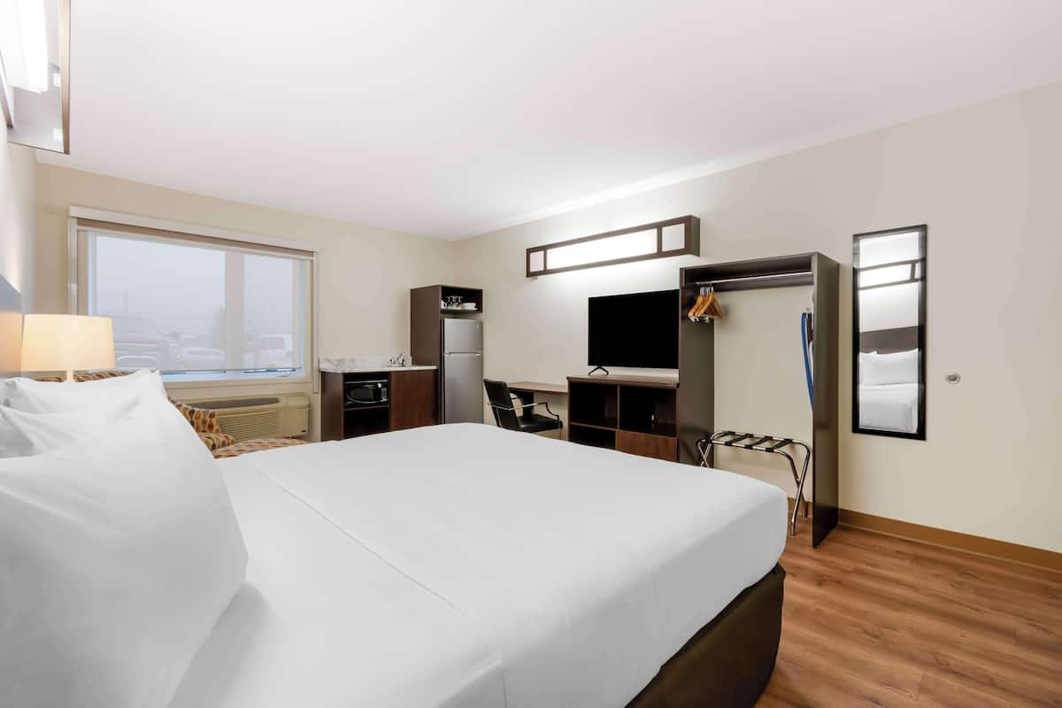A hotel room with a large bed, a desk, a TV, a wardrobe, and a window with a view of parked cars.