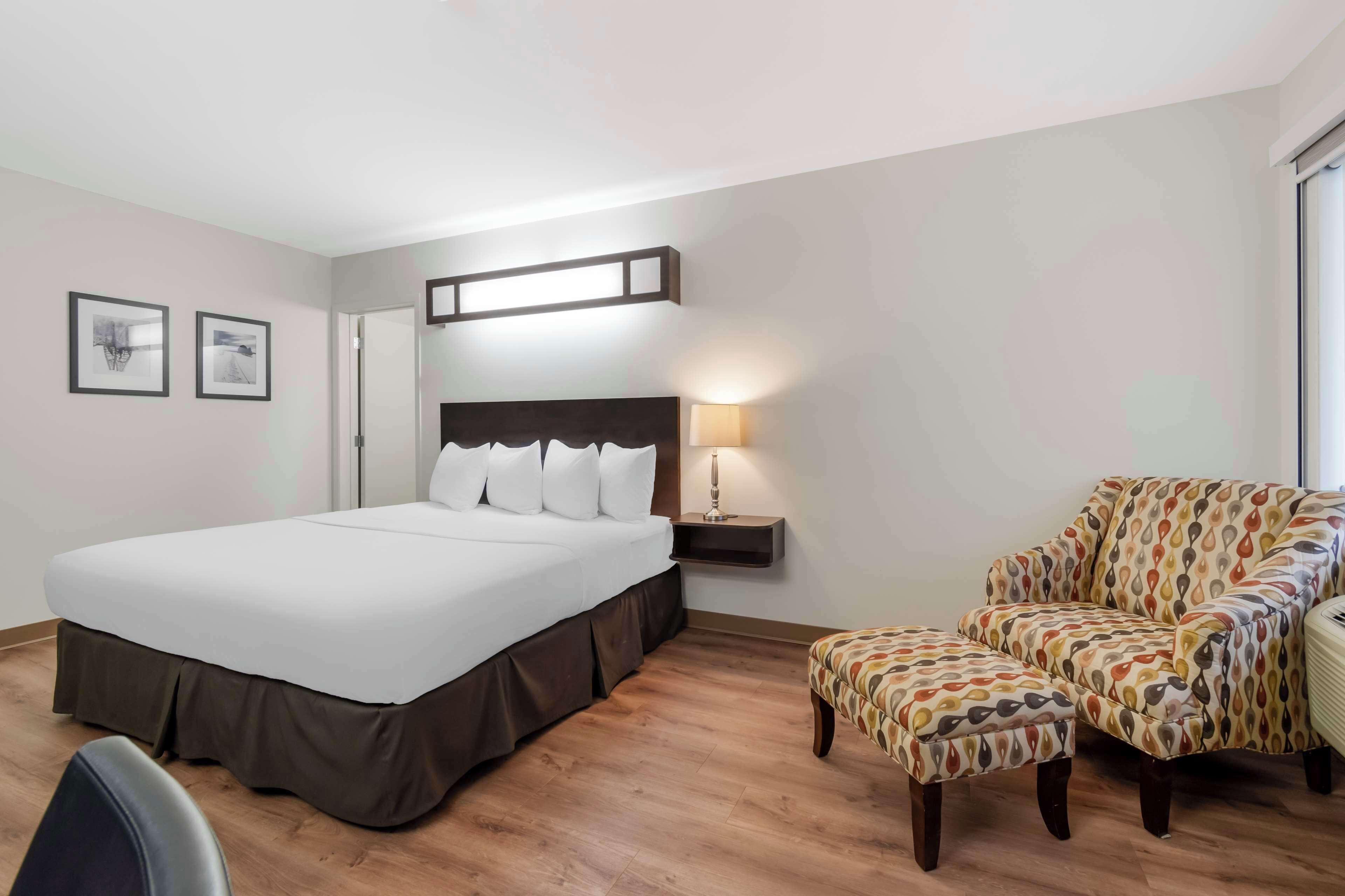 Ett hotellrum med en stor säng, en stol, ett skrivbord och en lampa.