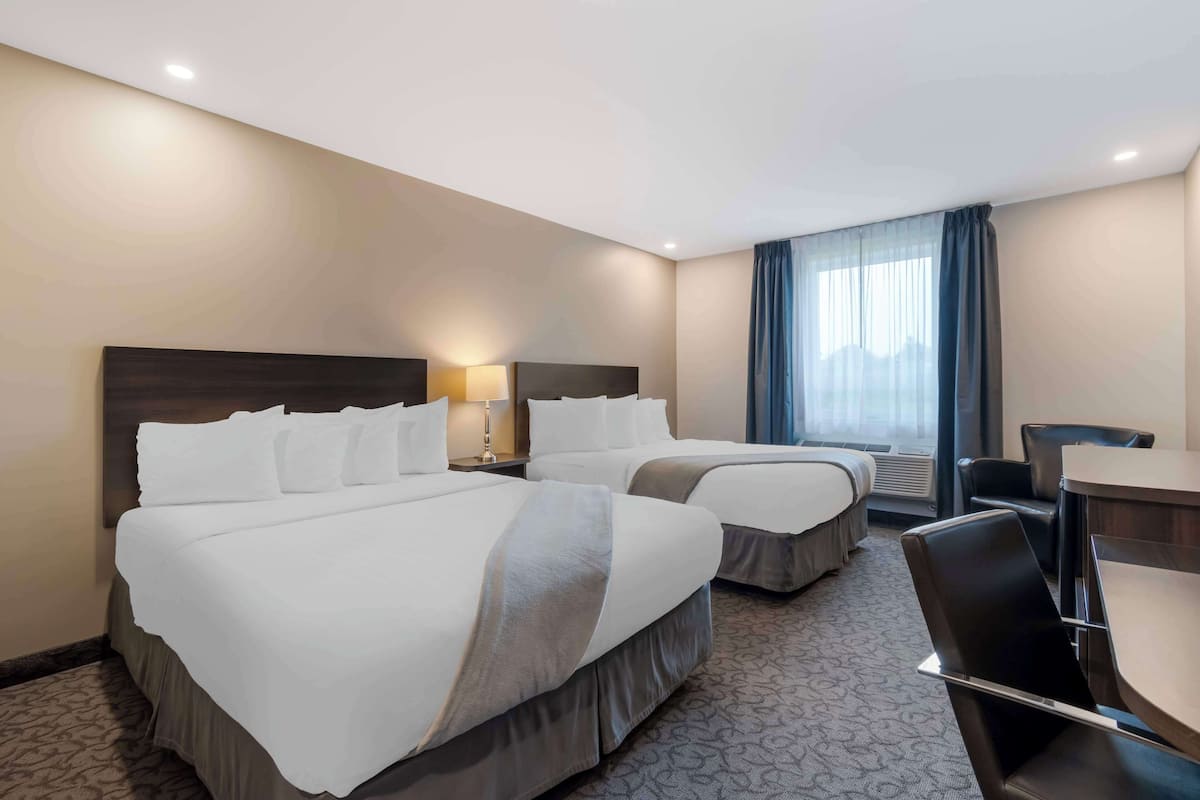 A hotel room with two beds, a desk, and a chair.