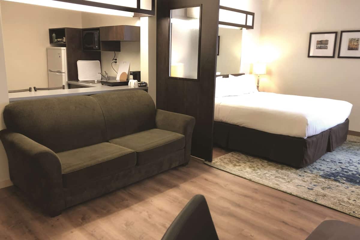 A hotel room with a sofa, a bed, a desk with a chair, a microwave, and a small refrigerator.