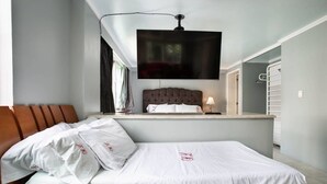 Et hotelværelse med en seng, et fjernsyn ophængt på væggen, et natbord med en lampe og et vindue med gardiner.