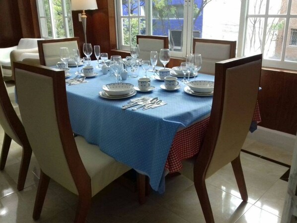 A dining table set for six with white chairs, blue tablecloth, and white plates.