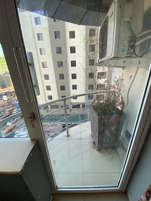 A balcony with a view of a multi-story building, a potted plant, and an air conditioning unit. - Ismarriot Hotel and Resort (Nairobi)